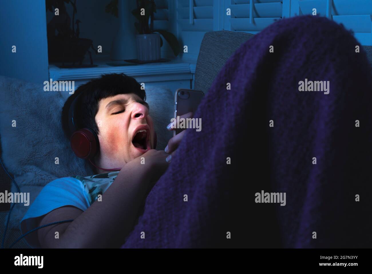 Müde Teenager auf seinem Handy im Bett gähnend. Spät in der Nacht, Schlaflosigkeit, Großbritannien Stockfoto