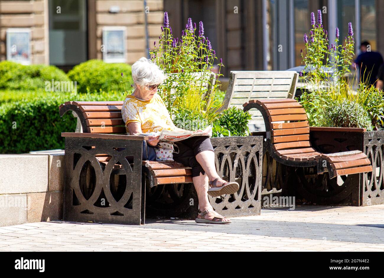 Dundee, Tayside, Schottland, Großbritannien. Juli 2021. UK Wetter: Warme Sonne über Nordostschottland mit Temperaturen bis zu 20 Grad Eine ältere Frau nimmt den Tag aus, um das Sommerwetter zu genießen, während sie auf einem Platz sitzt, der die Zeitung Evening Telegraph im Stadtzentrum von Dundee liest. Kredit: Dundee Photographics/Alamy Live Nachrichten Stockfoto