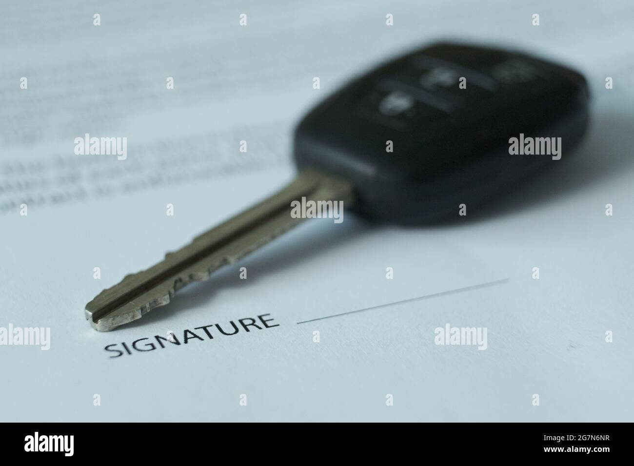 Es gibt einen Vertrag und Autoschlüssel auf dem Tisch, der Schwerpunkt liegt auf Schlüsseln und Unterschriften. Verschwommenes Bild. Stockfoto