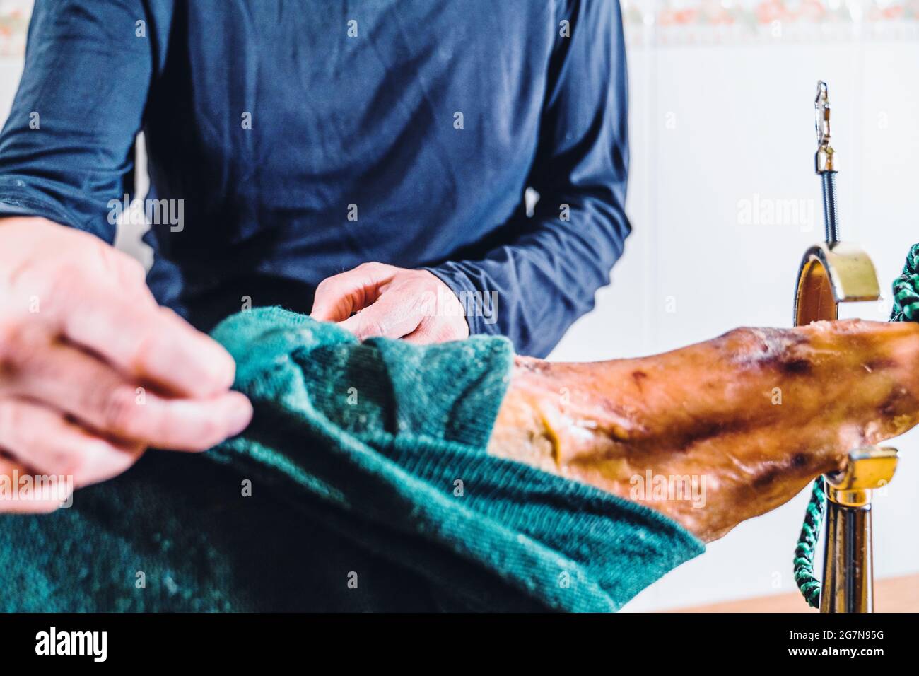 Anonymer Mann, der in der Küche zu Hause ein Bein Schinken zubereitet. Den Schinken in den Schinkenhalter stecken. Geschenk einer Schinkenschulter. Iberischer Schinken. Typisch spanisches F Stockfoto