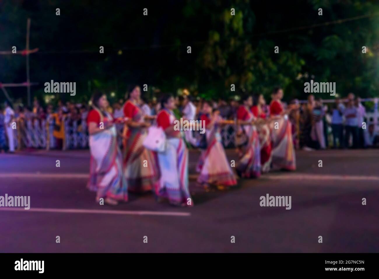 Verschwommenes Bild von bengalischen Hindu-Damen in rot-weißen Saris, traditionellen indischen Kleidern, gehen auf dem Durga Puja Karneval auf der Roten Straße in der Nähe Stockfoto