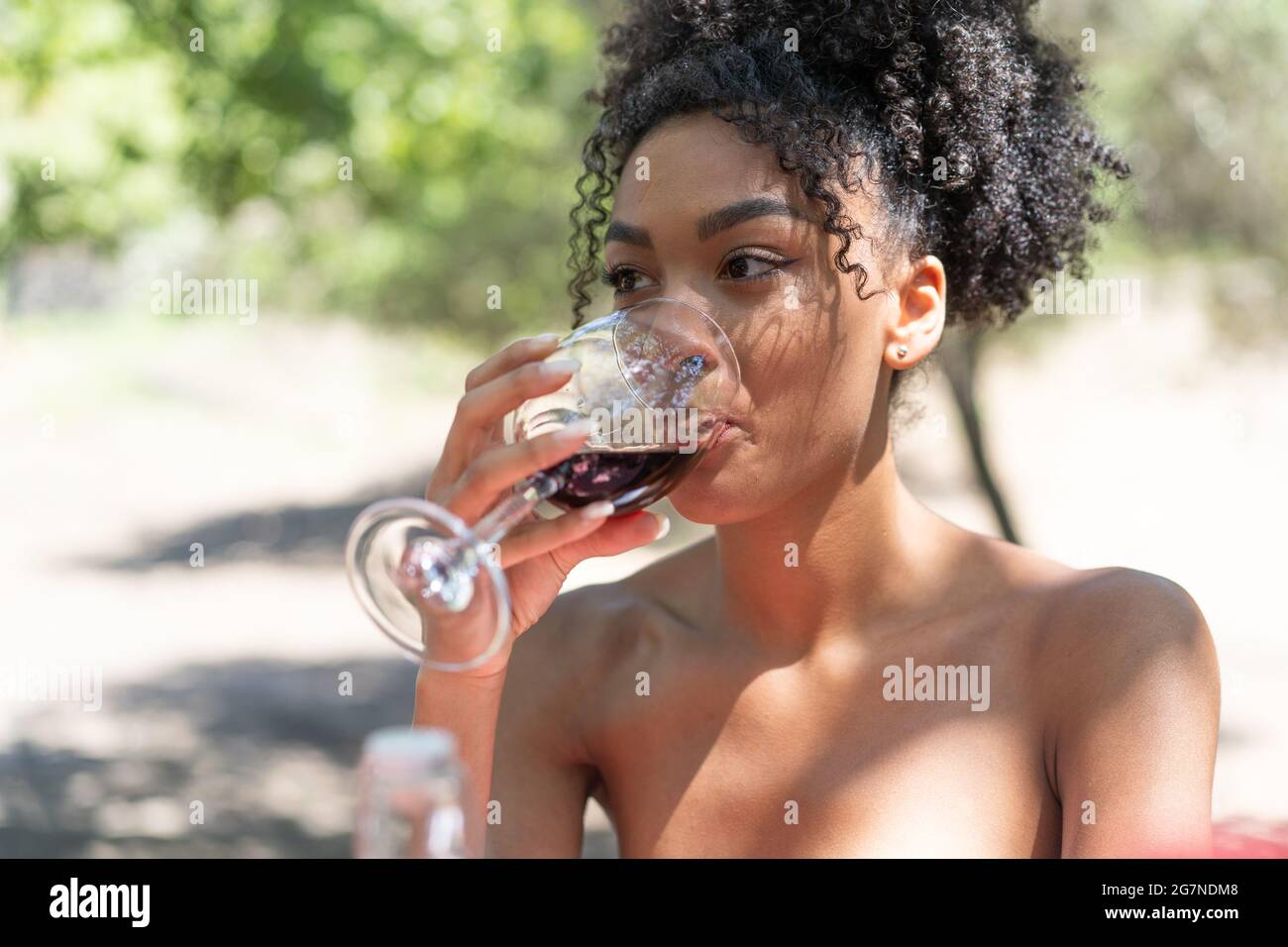 Junge Frau afrikanischer Abstammung, die auf dem Land Rotwein trinkt Stockfoto