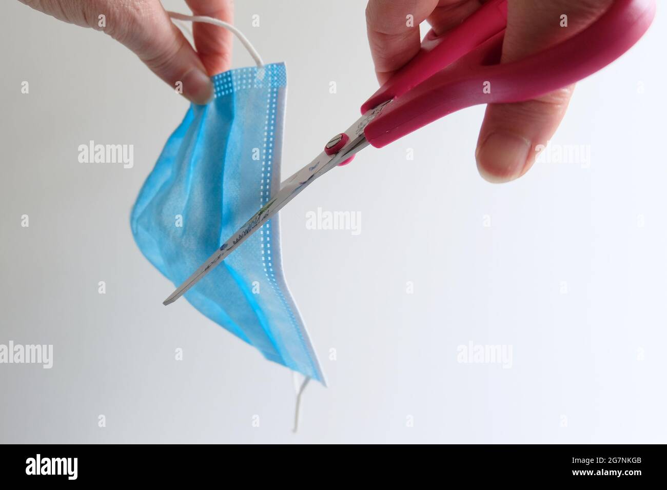 Hände eines reifen Erwachsenen, der eine Schere zu einer blauen Gesichtsmaske nimmt Stockfoto