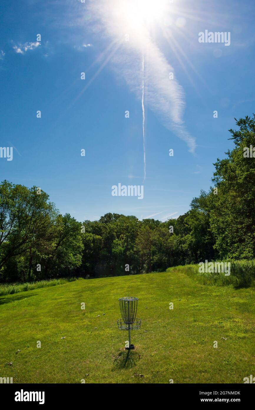 Sonnenlicht und ein Jet-Contrail scheinen auf ein sommerliches Disc-Golf-Tor zu verweisen und es hervorzuheben. Stockfoto