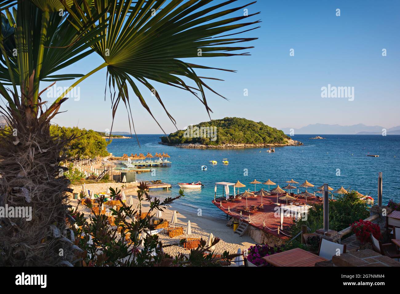 Wunderschöne Morgenlandschaft mit Sandstrand, Insel, Sonnenschirmen und blauem ionischem Meer an der albanischen Küste Stockfoto