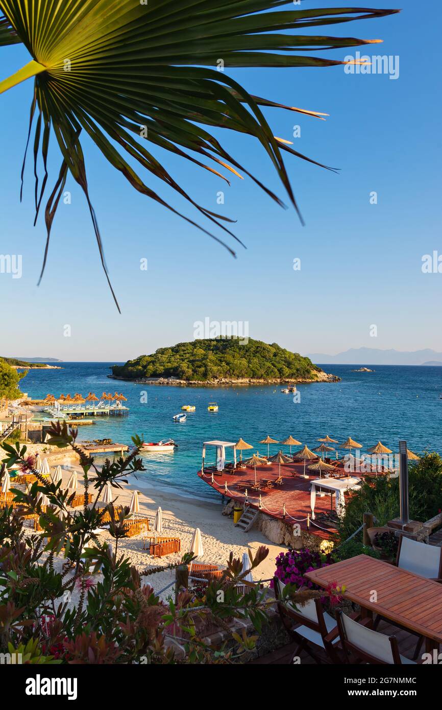 Wunderschöne Morgenlandschaft mit Sandstrand, Insel, Sonnenschirmen und blauem ionischem Meer an der albanischen Küste Stockfoto