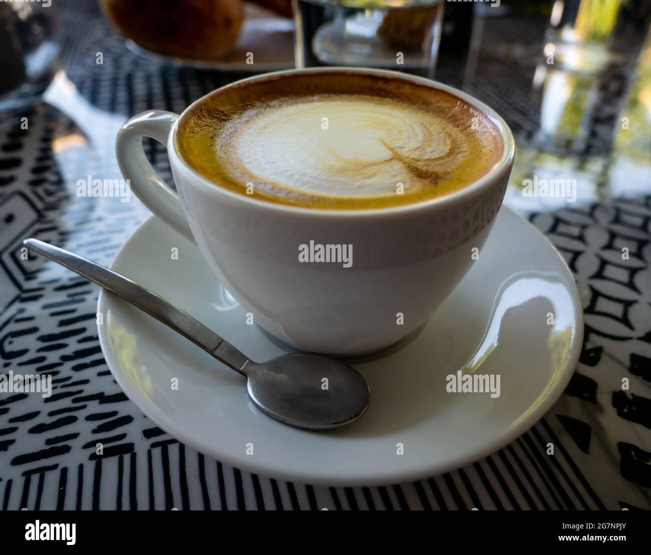 Nahaufnahme einer Tasse Cappuccino auf einem Teller mit einem Löffel auf dem Tisch in einem Café Stockfoto