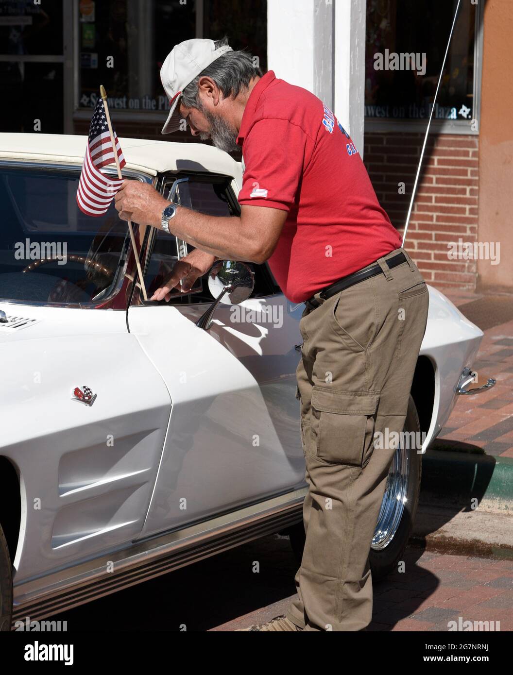 Ein Mann positioniert eine kleine amerikanische Flagge auf seiner klassischen Chevrolet Corvette aus den 1960er Jahren, die auf einer Automobilausstellung am 4. Juli in Santa Fe, New Mexico, ausgestellt wird. Stockfoto