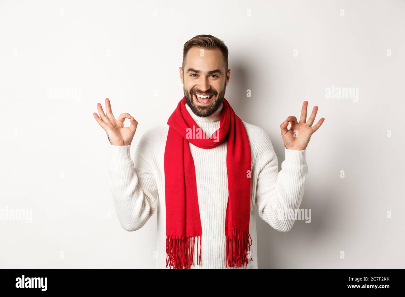 Winterurlaub und Shopping-Konzept. Aufgeregt Homosexuell Mann feiert weihnachten, zeigt okay Zeichen und lächelt selbstbewusst, über weiß stehen Stockfoto