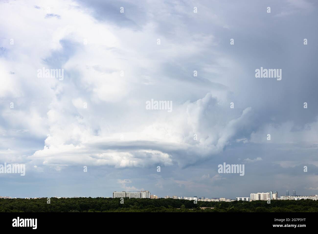 Graue Regenwolken mit Wirbeln über Stadt und Wald am Junitag Stockfoto