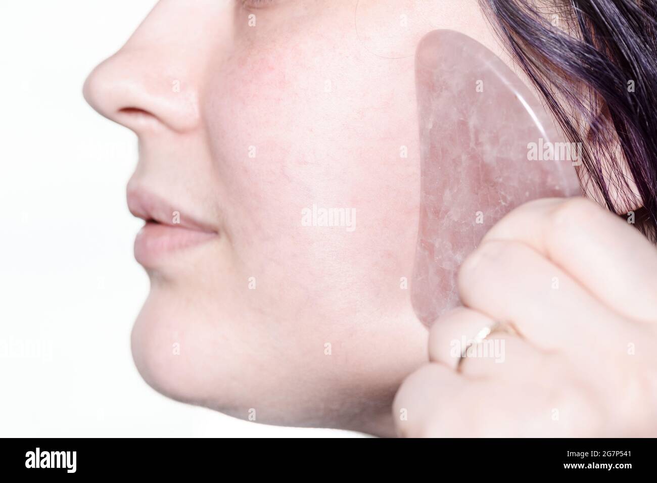 Frau massiert Wange mit Quarzkratzer in der Technik der traditionellen chinesischen Gua Sha Massage Stockfoto