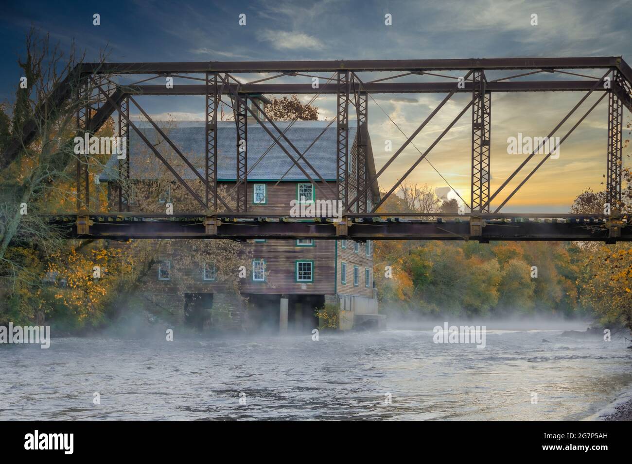 Altes, verlassenes Mühlenhaus mit einem verlassenen Zug, der das Wasser überquert und bei Sonnenaufgang nebligen Nebel vom Wasser abgibt, in New Jersey Stockfoto