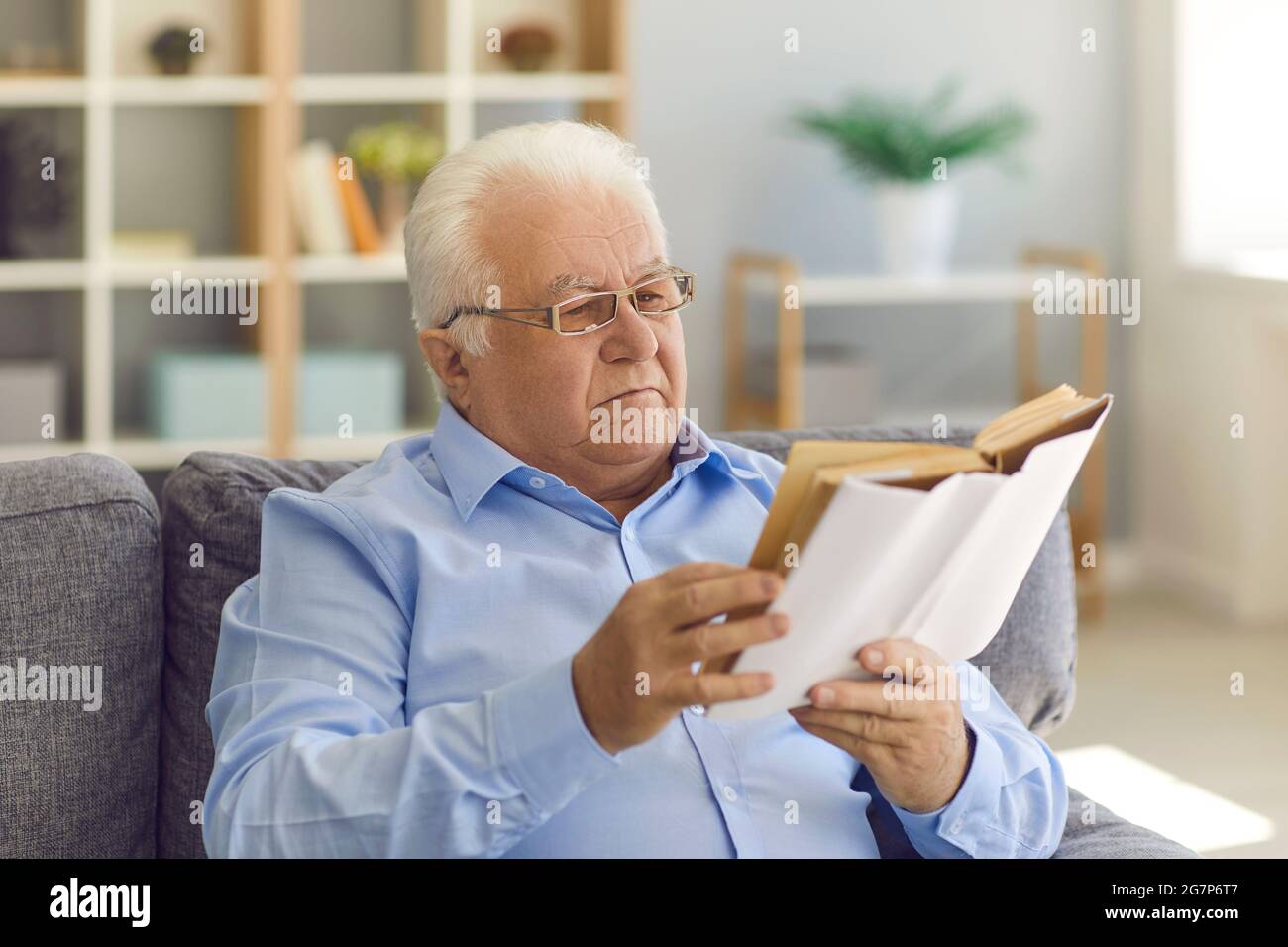 Ernsthafter älterer Mann in neuen Brillen sitzt auf der Couch und genießt ein gutes Buch Stockfoto