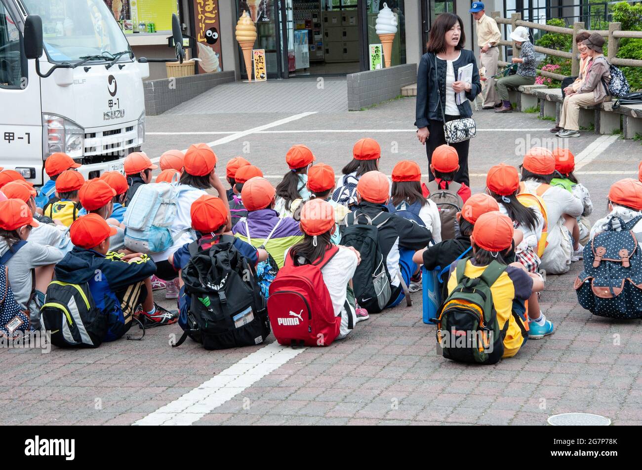 Eine Gruppe von Schülern, die die gleichen leuchtend orangefarbenen Hüte tragen, mit einem Lehrer auf einer Exkursion in Japan. Stockfoto