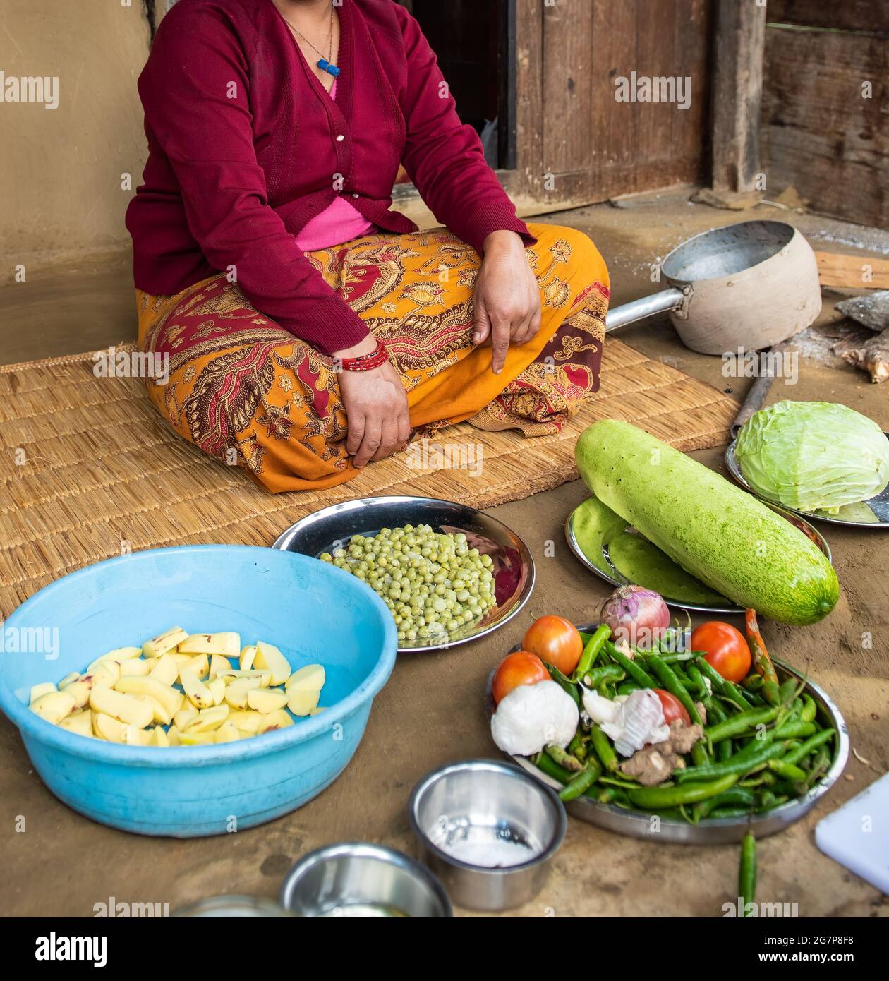 Eine Frau in farbenfroher Kleidung sitzt vor ihrem Haus und bereitet in Nepal Gemüse zu. Stockfoto