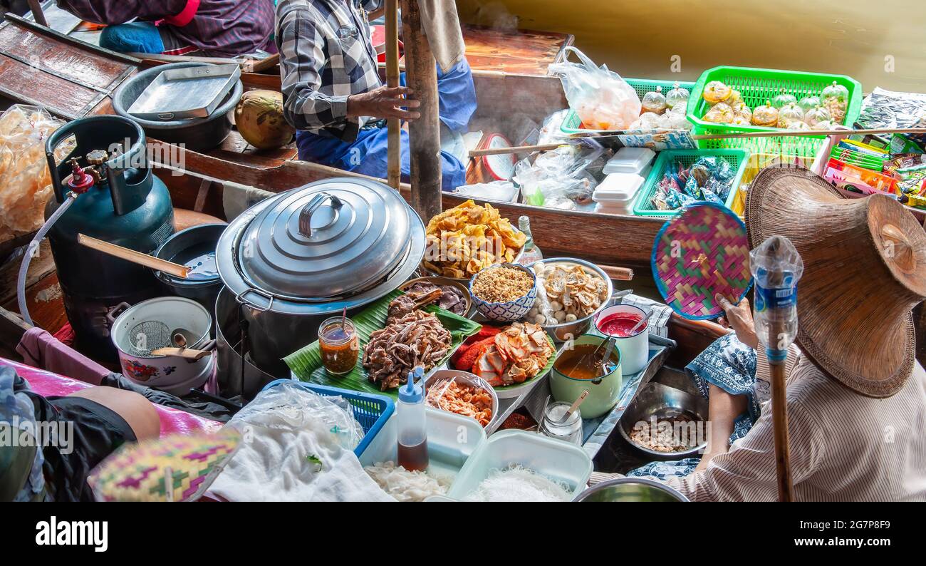 Frau mit Strohhut in einem Boot, die Gemüse und Obst auf einem schwimmenden Markt in Thailand verkauft, verbunden mit einem zweiten Boot. Stockfoto