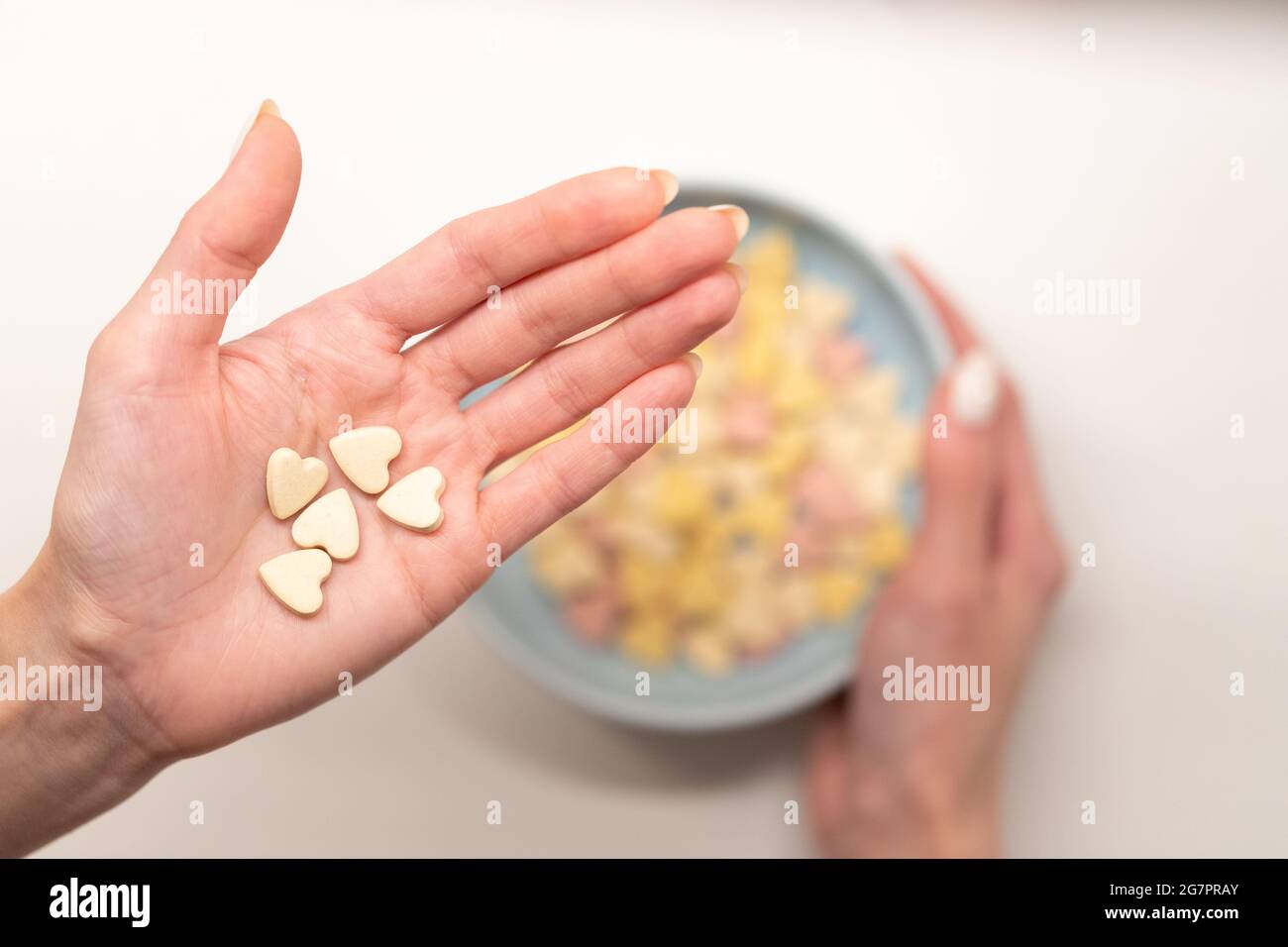 Gesundes Frühstück am Morgen: Frau Hand hält leckere Flocken über Schüssel mit Müsli im weiblichen Arm Stockfoto