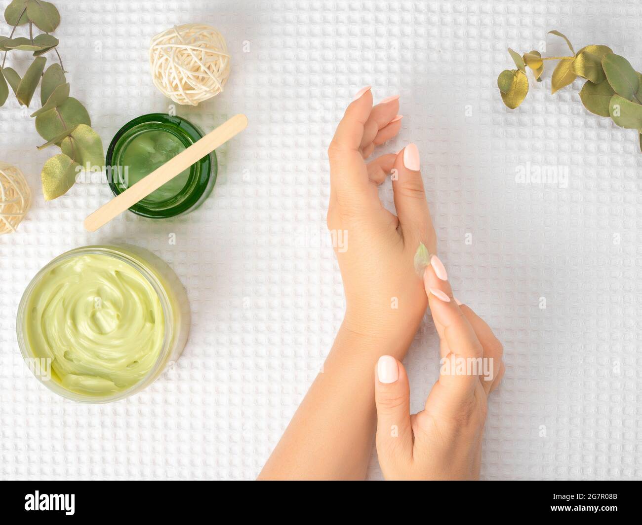 Draufsicht und flacher Lay von Frau, die Creme auf den Händen über ein weißes Handtuch mit Kosmetikprodukten hält - Avocado-Öl, Creme und Bambusstock. Draufsicht Stockfoto