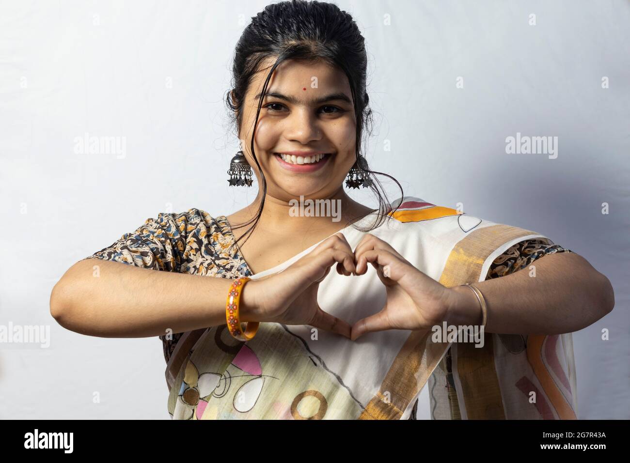Isoliert auf weißem Hintergrund zeigt ein indisches Weibchen in Saree eine Liebesgeste mit lächelndem Gesicht auf weißem Hintergrund Stockfoto