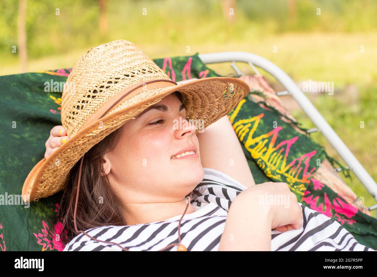 Lächelndes Mädchen in Strohhut und gestreiftem T-Shirt liegt auf einem Kinderbett im Freien Stockfoto