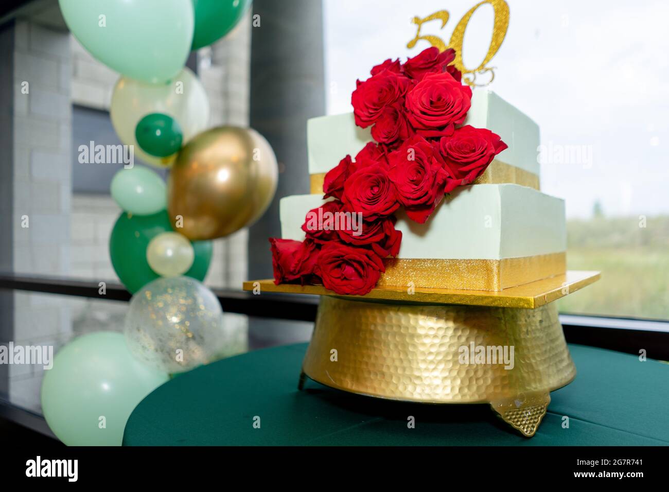 Festlicher Kuchen zum 50. Geburtstag mit roten Rosen und goldenen Streifen und bunten Luftballons Stockfoto