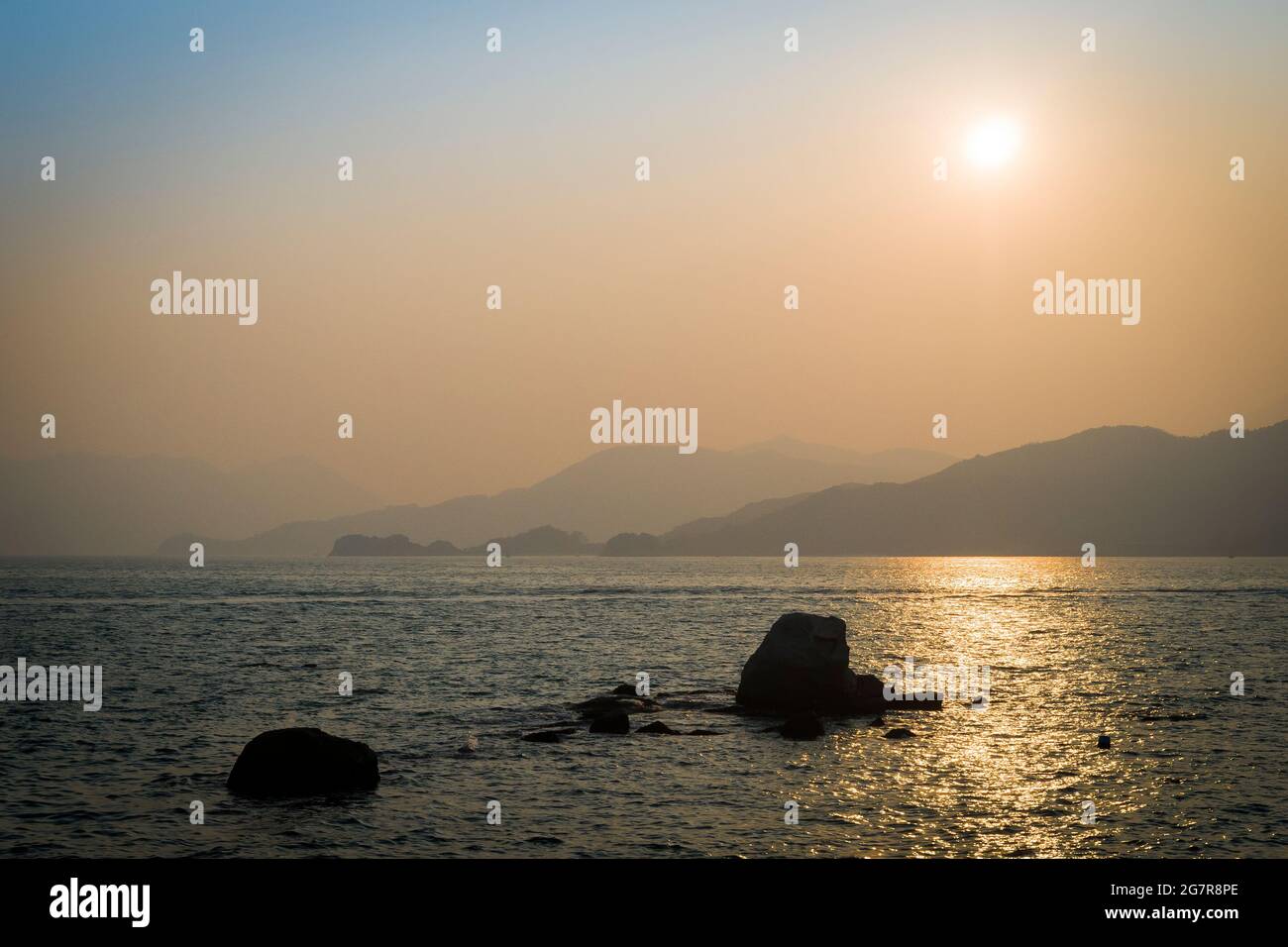 Die Sonne sinkt in die Smog-Schicht, die vom Festland China über die Insel Lantau von Peng Chau, einer der Outlying Islands von Hongkong, kommt Stockfoto