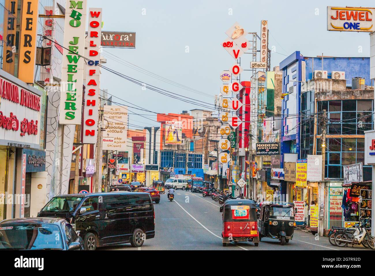 Blick auf die geschäftige Hauptstraße mit Vogue Juweliergeschäften, Auto-Rikschas, Ladenfronten und bunten Plakatwänden, Negombo, Sri lanka Stockfoto