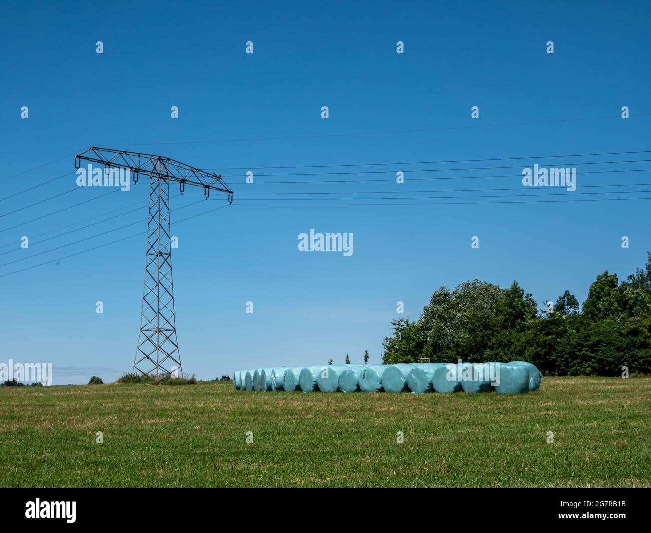 Strommast auf dem Feld mit Heuballen Stockfoto