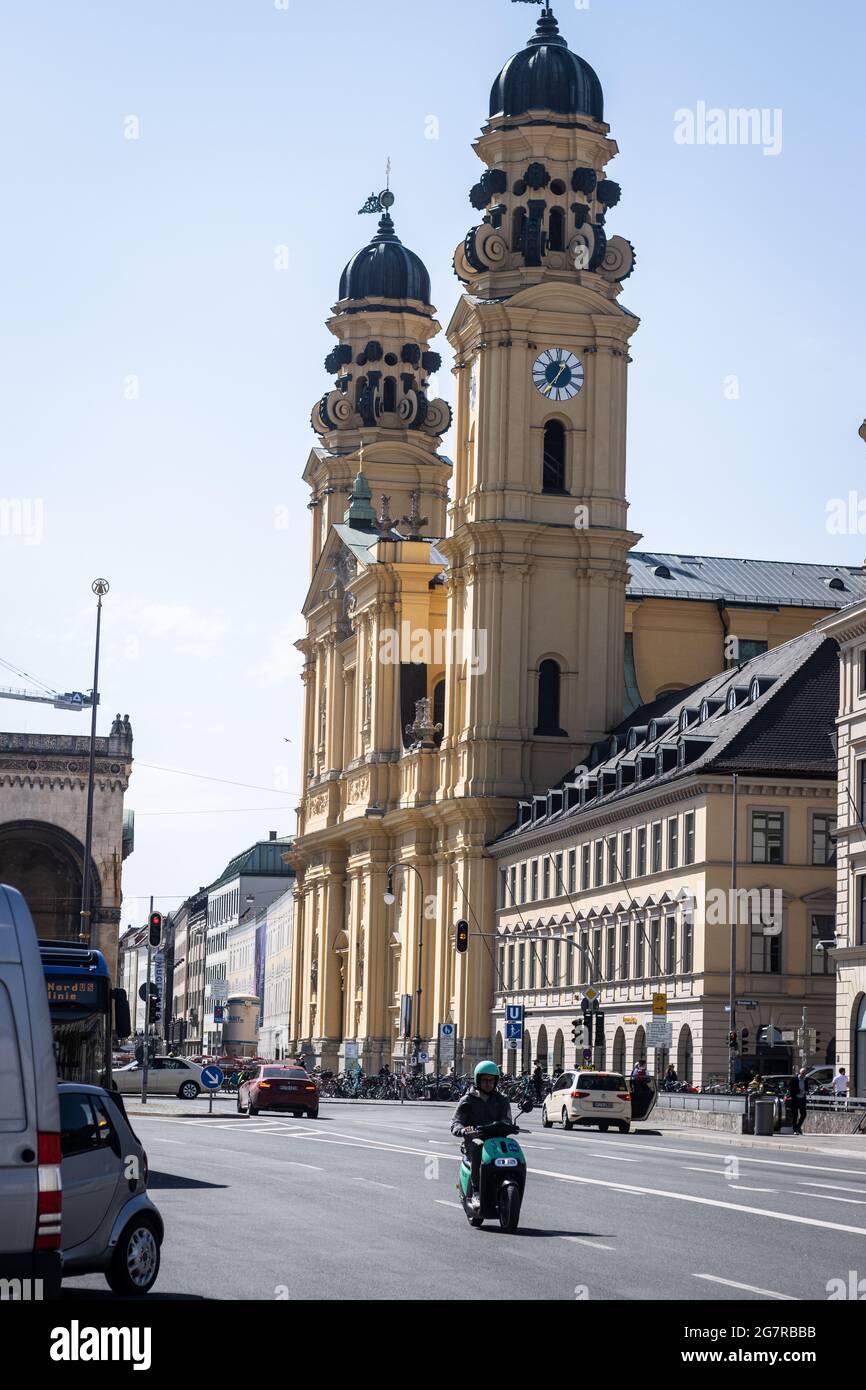 MÜNCHEN, DEUTSCHLAND - 12. Jun 2021: Ein Moped-Fahrer in den Straßen von München mit der Theatinerkirche im Hintergrund Stockfoto