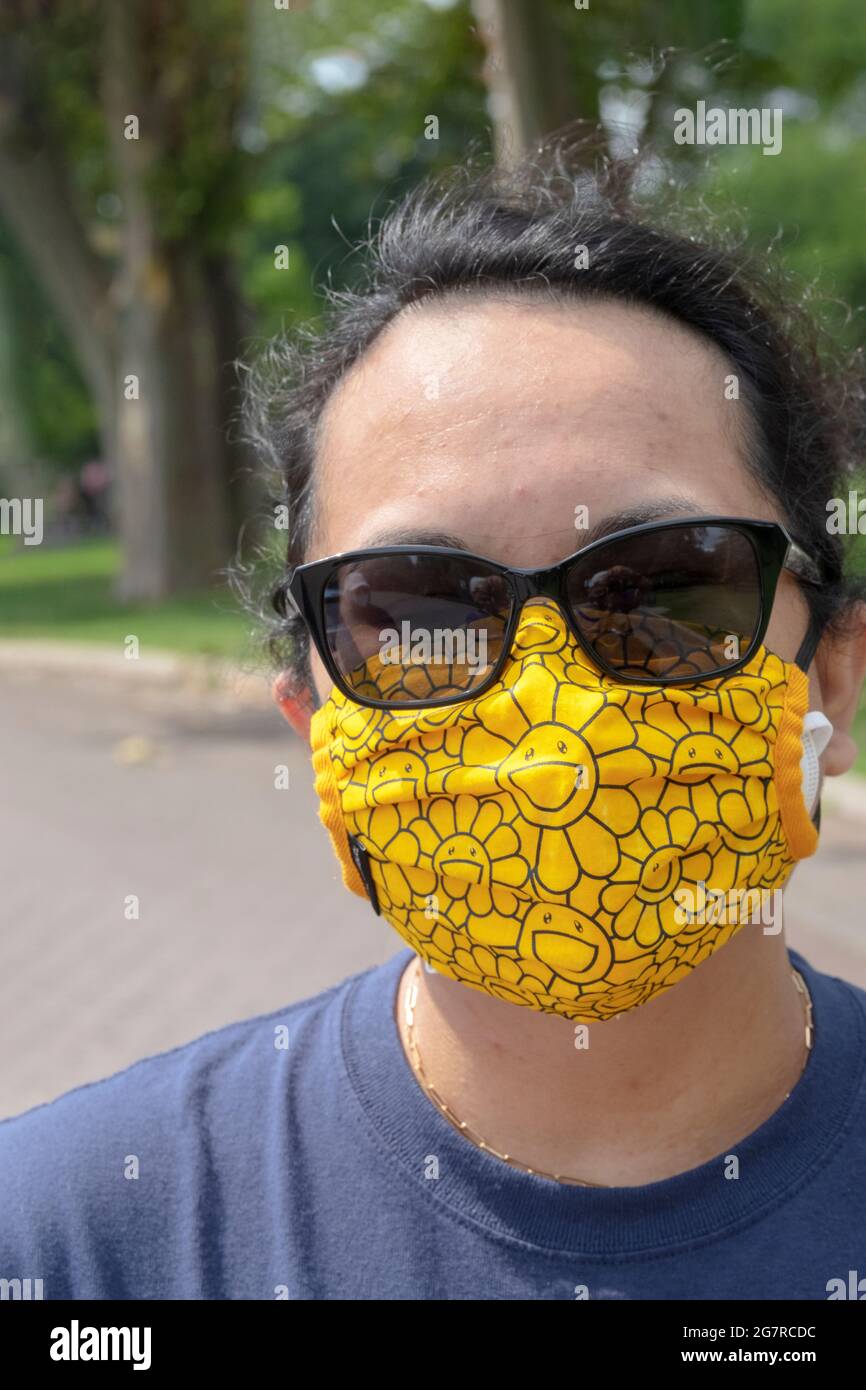 Eine Frau mit einer gelben Murakami Gesichtsmaske in einem Park in Queens New York City. Stockfoto