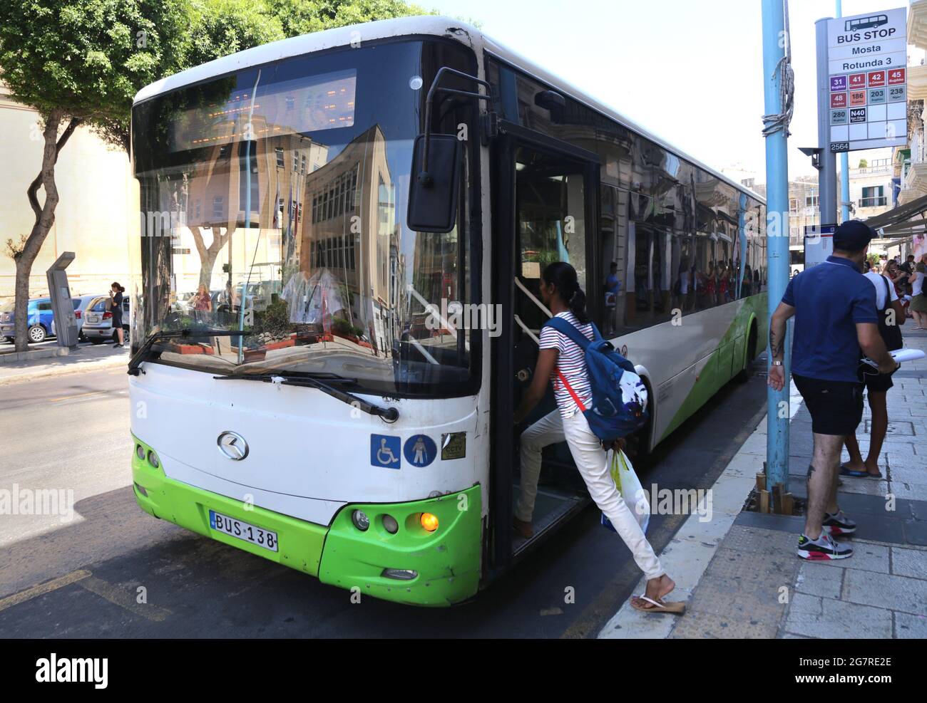 Mosta. Malta. Grün und weiß Öffentliche Verkehrsmittel Bus an der Haltestelle. Junge Frau, die an Bord geht. Stockfoto