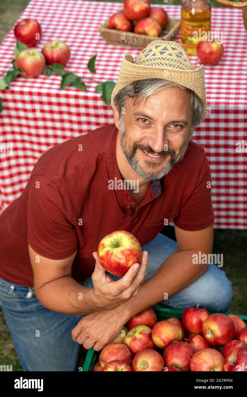 Charismatischer, reifer Bauer mit rotem Apfel und Blick auf die Kamera. Konzept Für Gesunde Ernährung. Bauer pflückt Äpfel in einem Obstgarten. Stockfoto