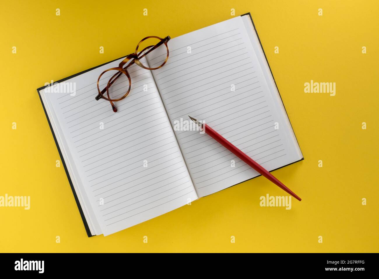 Liniertes Notizbuch mit Vintage-Stift in Rot mit Feder und alter Brille, isoliert auf gelbem Hintergrund, Kopierbereich Stockfoto