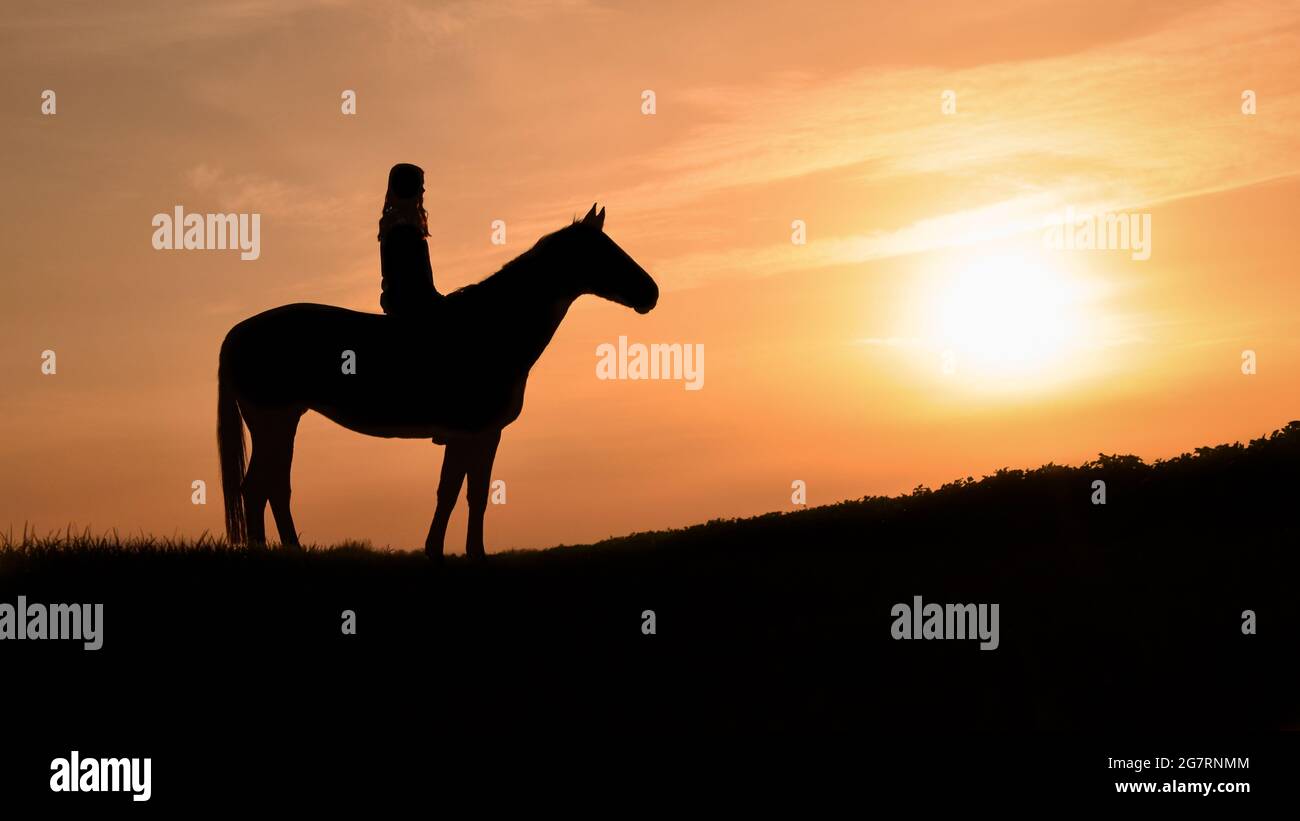 Ein Mädchen mit ihrem Pferd vor einer verträumten Sonnenuntergangslandschaft Stockfoto