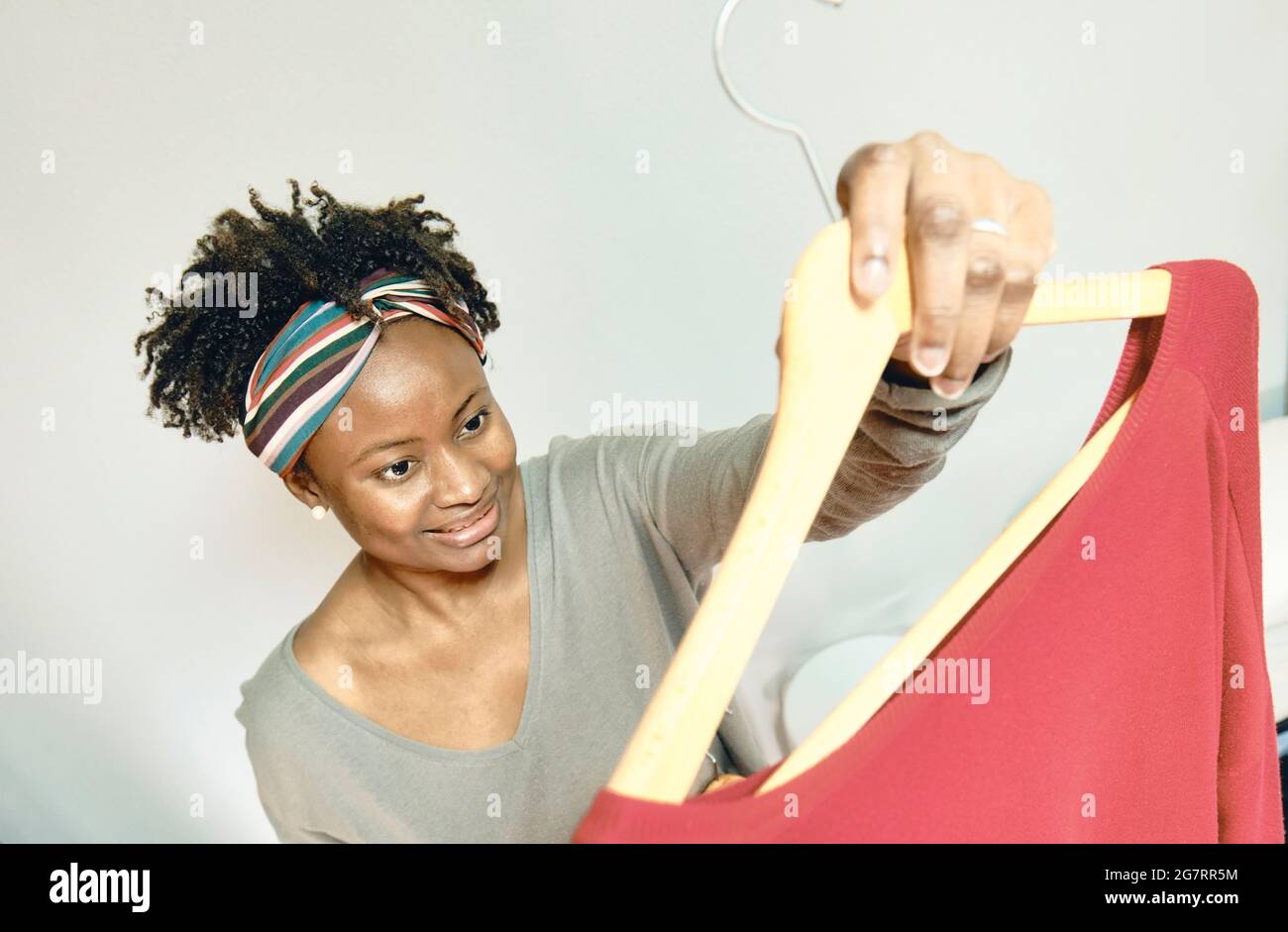 Porträt einer jungen schwarzen Frau mit afro Frisur mit Kleidung auf Kleiderbügeln innen zu Hause. Lifestyle-Konzept. Stockfoto