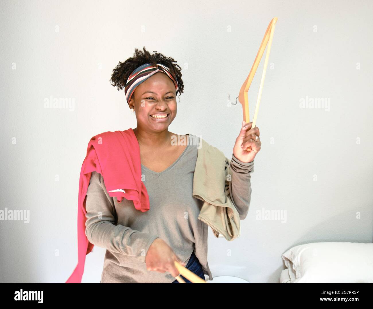 Porträt einer jungen schwarzen Frau mit afro Frisur mit Kleidung auf Kleiderbügeln innen zu Hause. Lifestyle-Konzept. Stockfoto