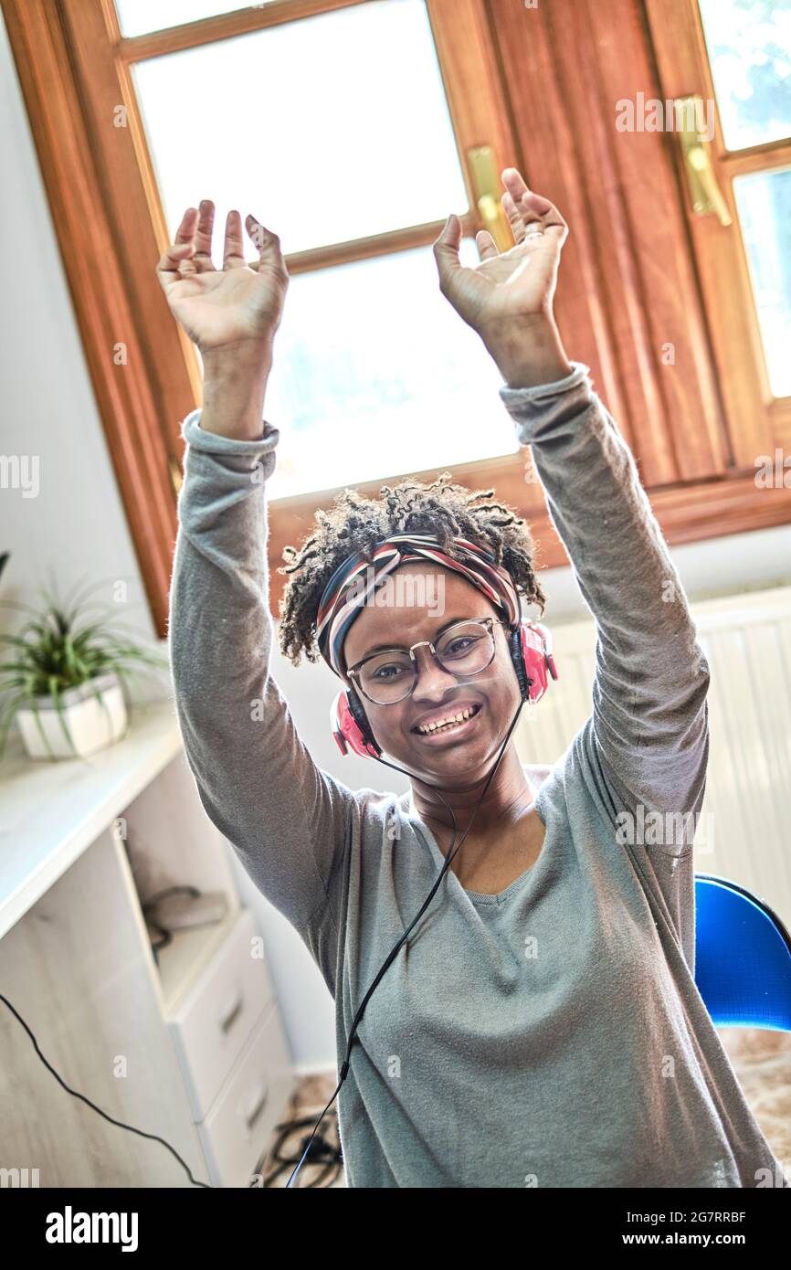 Junge schwarze Frau mit Afro-Frisur, die in einem Haus mit Kopfhörern Musik hört. Lifestyle-Konzept. Stockfoto