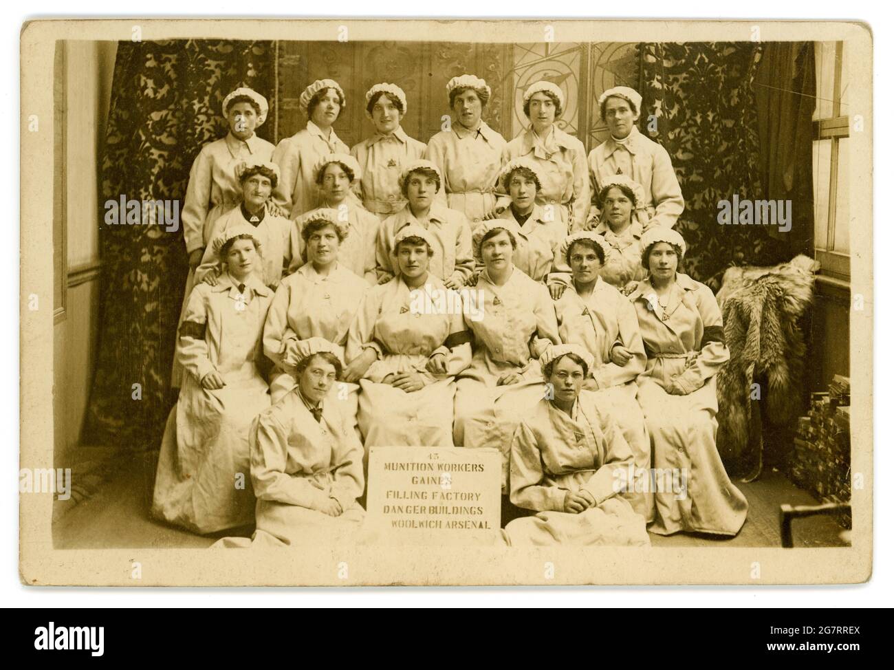 Postkarte aus der Zeit des 1. Weltkriegs mit Munitionsarbeitern, die in einem gefährlichen Job arbeiten, da das Schild auf der Vorderseite des Gruppenfotos zeigt, dass „Munition Workers Gaines Filling Factory Dangerous Buildings Woolwich Arsenal“ diese Munitionetten tragen Abzeichen „on war Service“. Postkarte datiert / veröffentlicht 1917, Woolwich, London, Großbritannien im Zusammenhang mit Artilleriemunition aus dem Ersten Weltkrieg waren 'gaines' instabile Sprengstoffe, die oft als Grundierung oder Zünder in Granaten verwendet wurden, meist in Verbindung mit anderen Sprengstoffen. Der Arsenal Football Club wurde 1886 als Munition Workers' Team aus Woolwich gegründet. Stockfoto