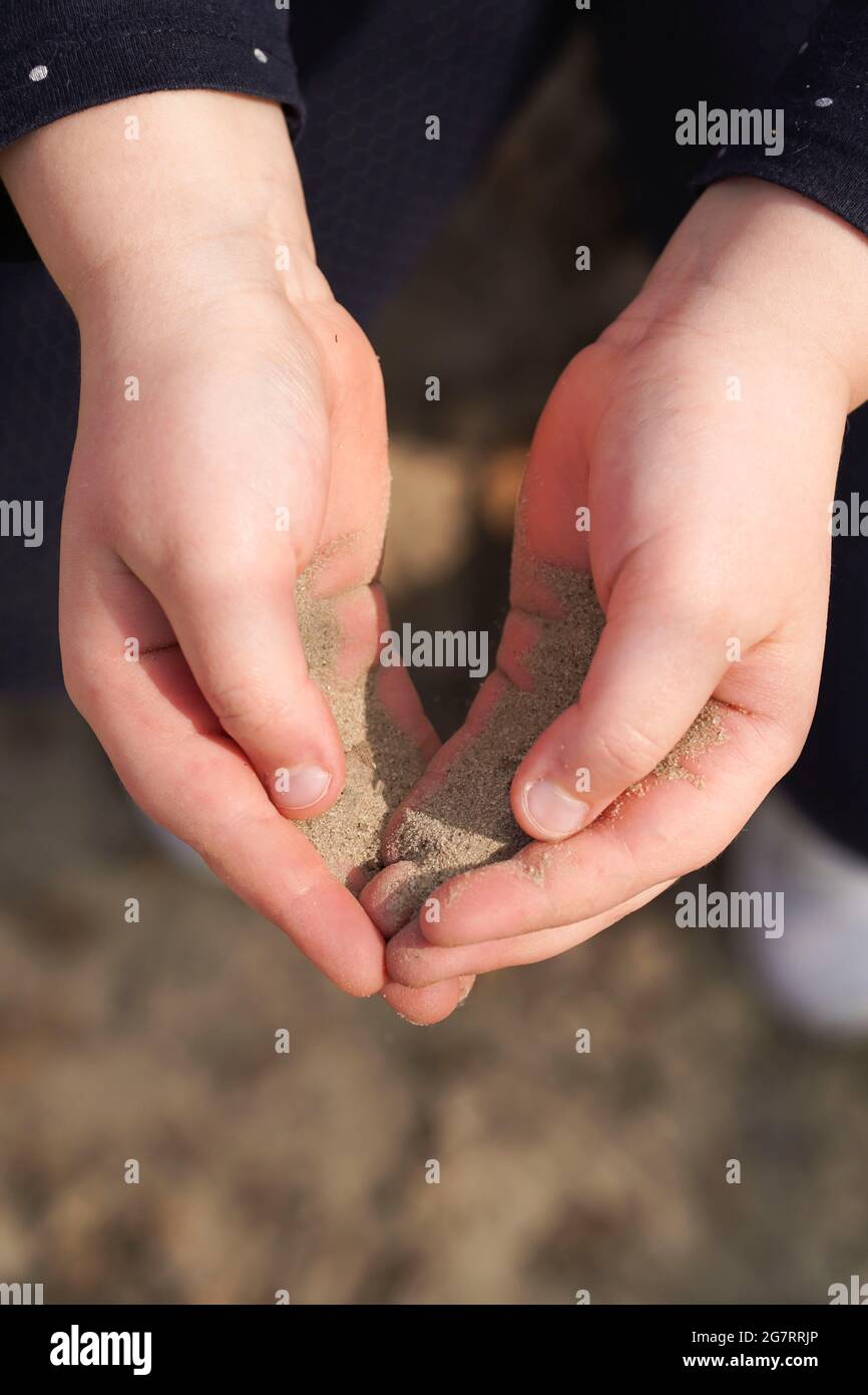 Kind hält Sand in den Händen. Sand durch seine Finger. Stockfoto