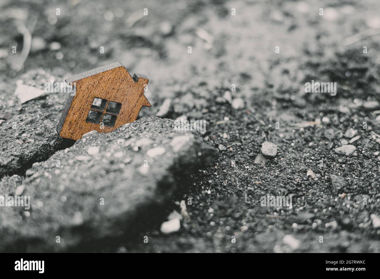 Zerstörung von Wohngebäuden und Erdbeben-Konzept . Holzspielzeughaus in einen Riss in der Erde gefallen. Stockfoto