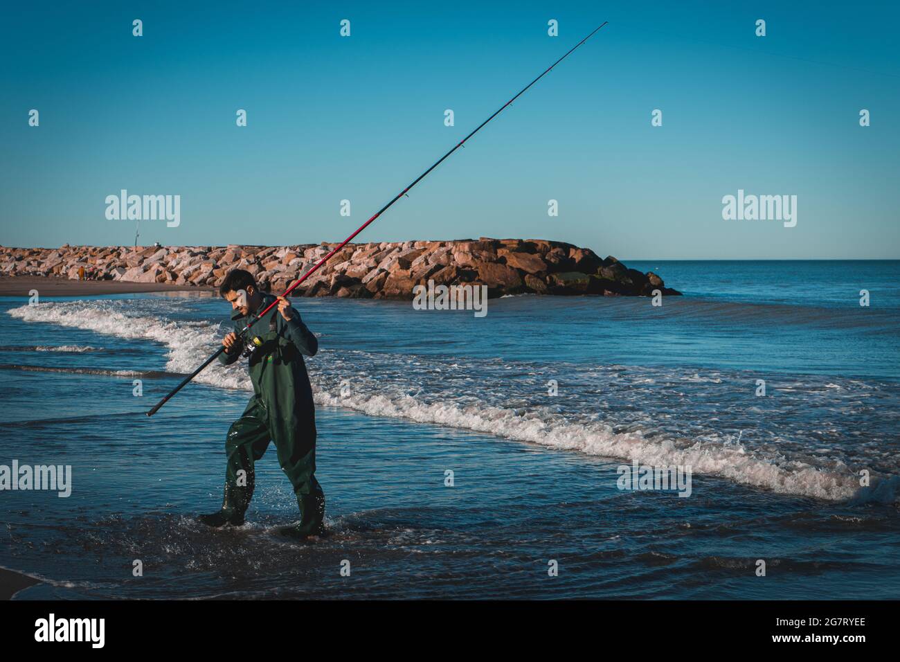 Der junge Argentinier versucht sein Glück beim Fischen zum ersten Mal am Meer während des Sonnenuntergangs Stockfoto