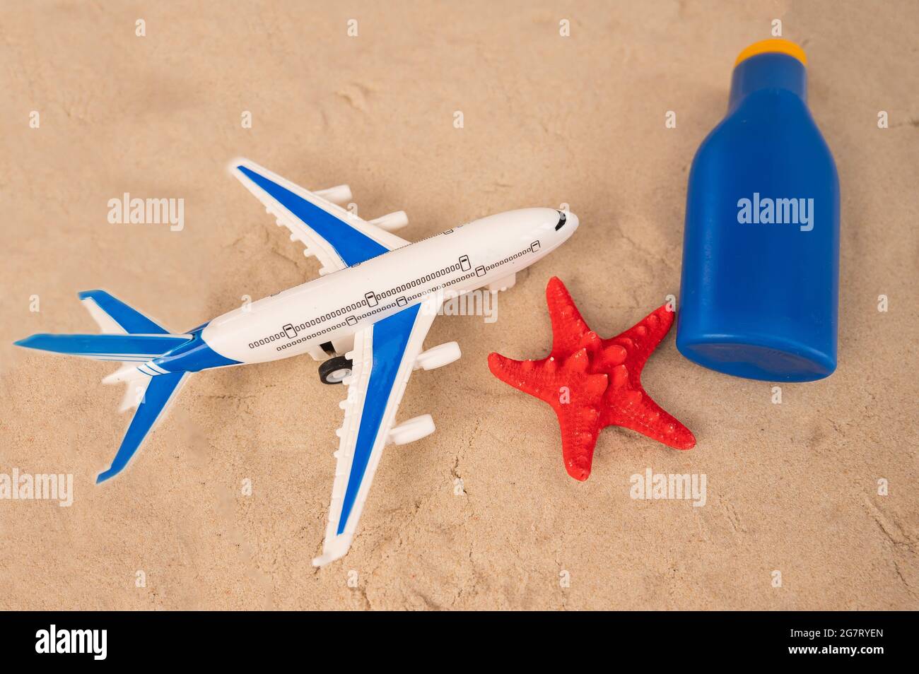 Flugzeugmodell roter Seesterne und ein Rohr mit Sonnencreme auf dem Sand. Urlaubskonzept am Meer. Stockfoto