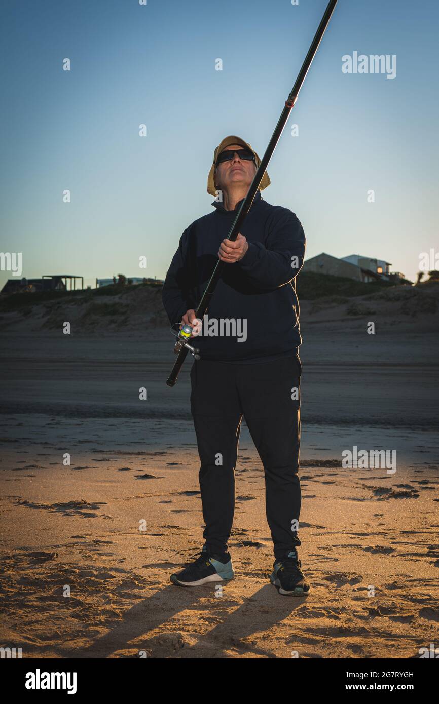 Vertikale Aufnahme eines erfahrenen Fischers am Ufer während des Sonnenuntergangs, der sich darauf vorbereitet, einige Fische zu fangen Stockfoto