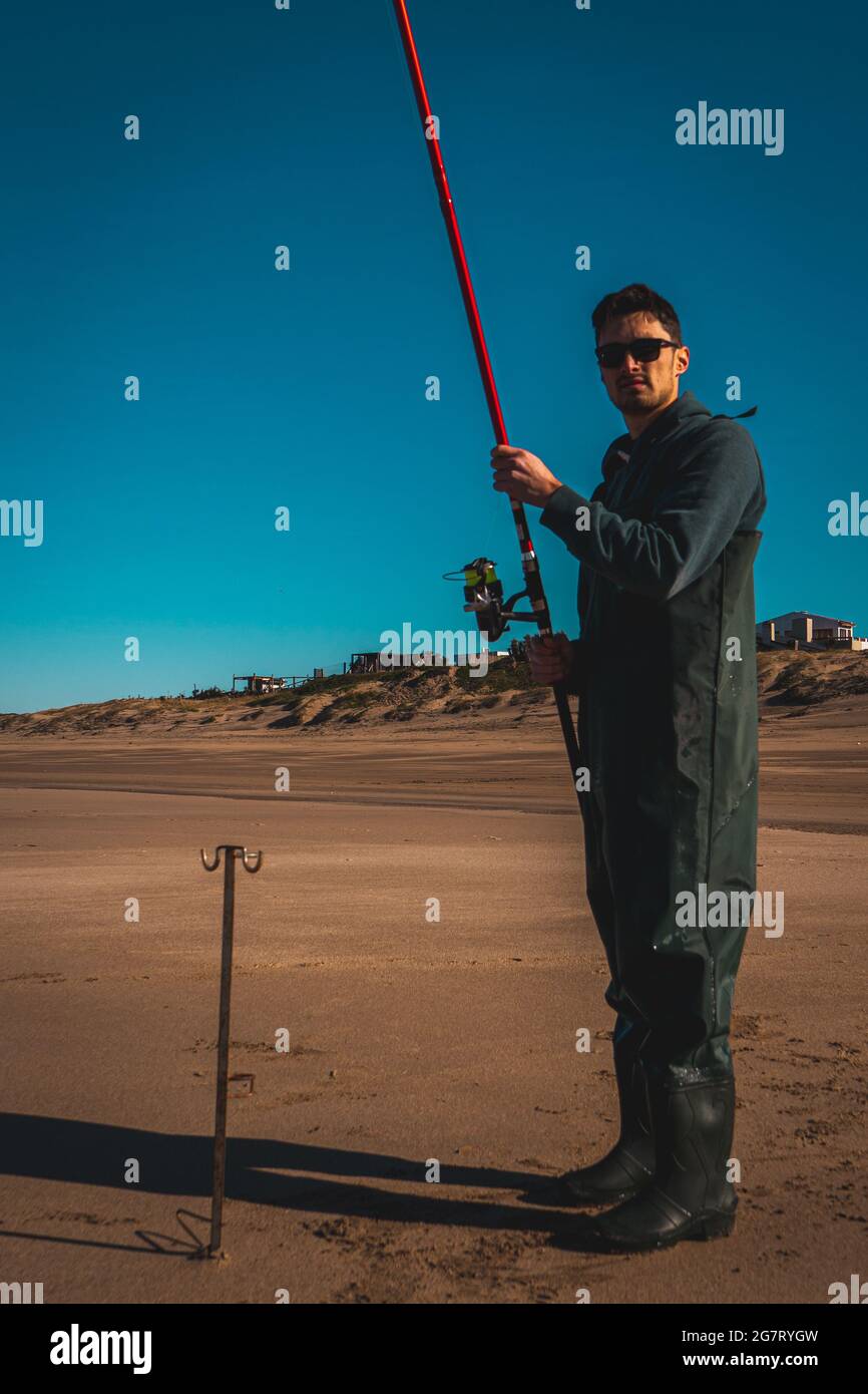 Vertikale Aufnahme eines coolen argentinischen Typen mit Sonnenbrillen am Strand, Angeln während des Sonnenuntergangs Stockfoto