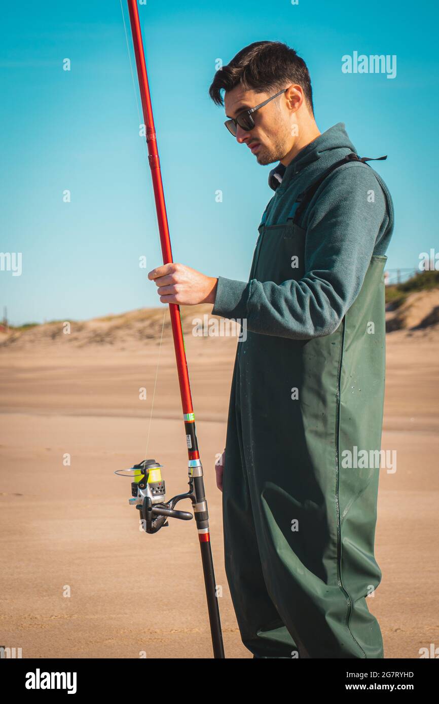 Vertikale Aufnahme eines jungen argentinischen Fischers mit Sonnenbrille und seinem Angelstock am Strand Stockfoto