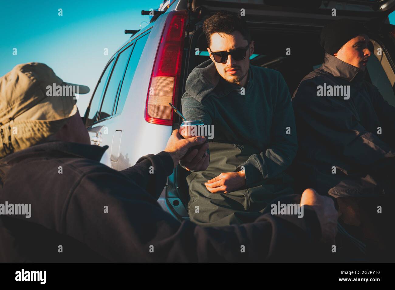 Gruppe argentinischer Männer, die sich nach dem Angeln am Strand entspannen und während des Sonnenuntergangs Bier trinken Stockfoto
