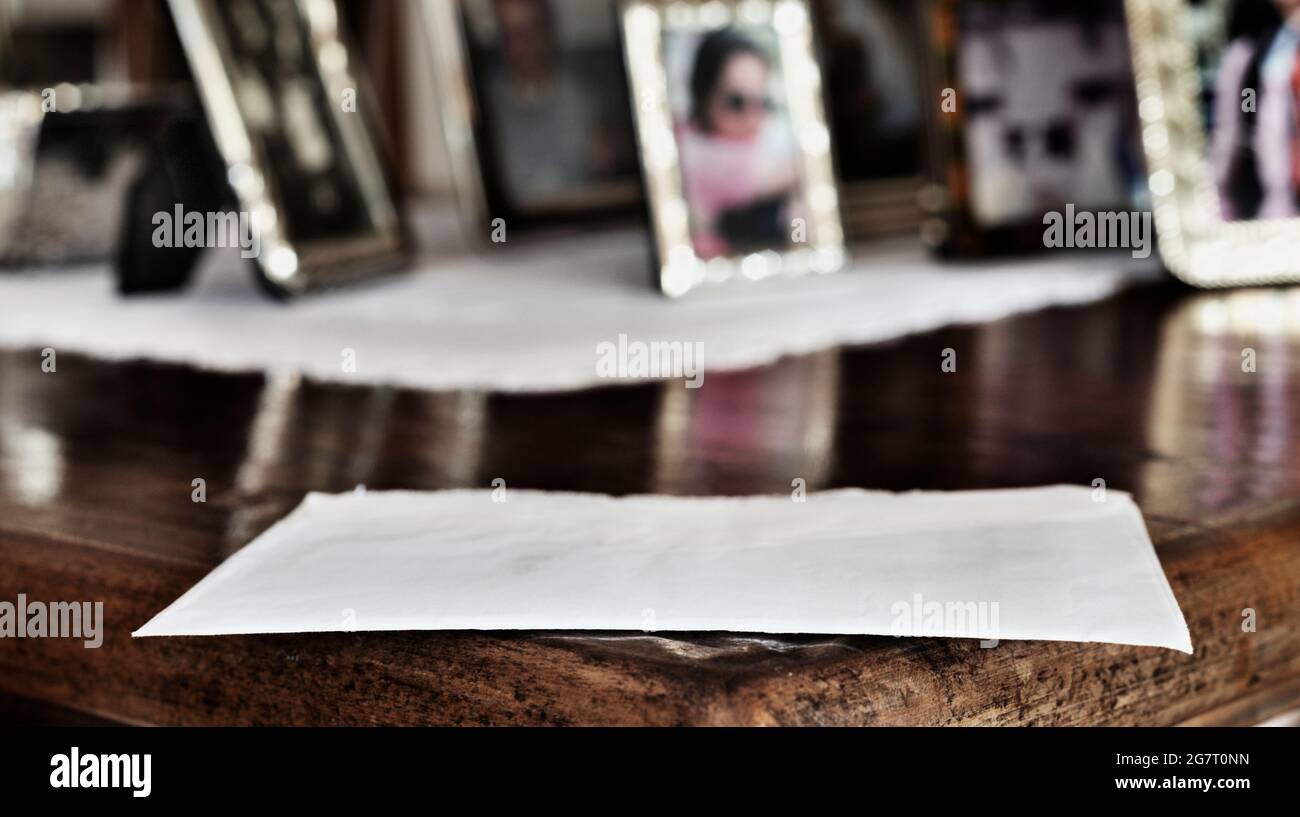 Weißer geschlossener Umschlag auf Holztisch, im Hintergrund mehrere silberne Fotorahmen Stockfoto