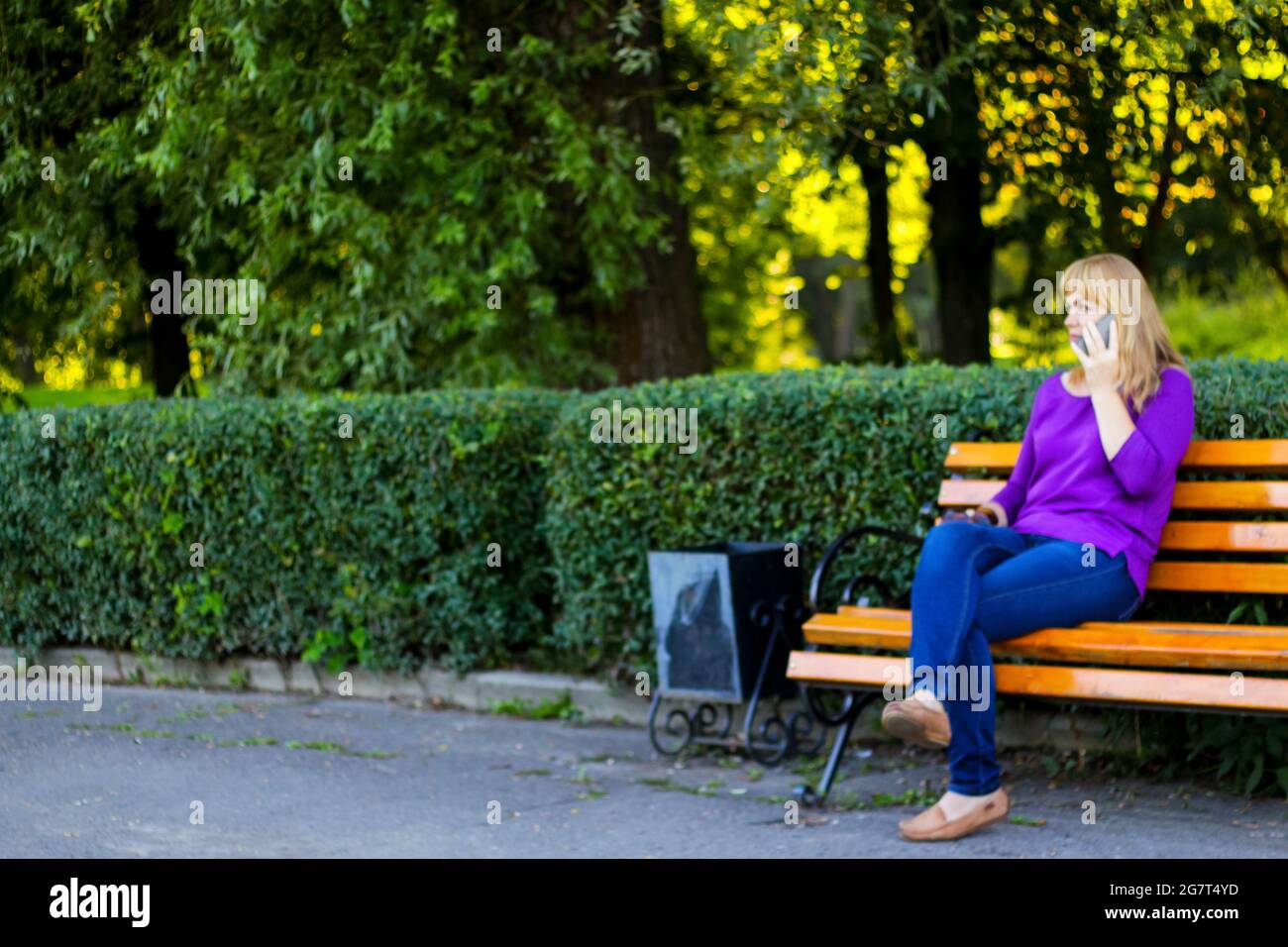 Unschärfe-Eleganz kaukasische blonde Frau reden, sprechen auf dem Telefon draußen, im Freien. 40-jährige Frau in lila Bluse im Park. Erwachsene Frauen usin Stockfoto