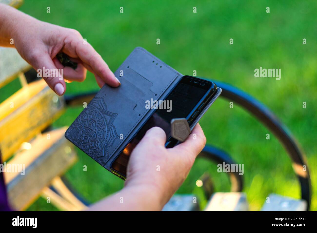 Unschärfe-Effekte bei Nahaufnahme von weiblichen Händen, die sich außerhalb des Telefons berühren. Frau in lila Bluse mit Smartphone, während sie auf einer Bank im Park sitzt. Co Stockfoto