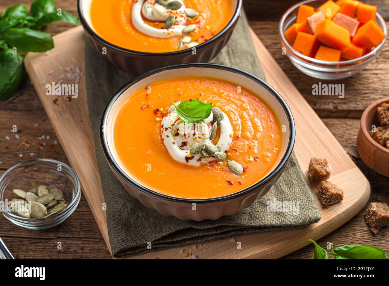 Kürbiscremesuppe mit Creme und Kürbiskernen auf braunem Holzgrund. Stockfoto